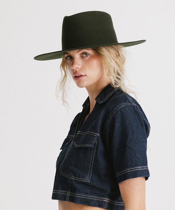 Woman wearing a dark green wide brim felt hat with a triangle crown and a denim jacket against a plain background #color_dark green
