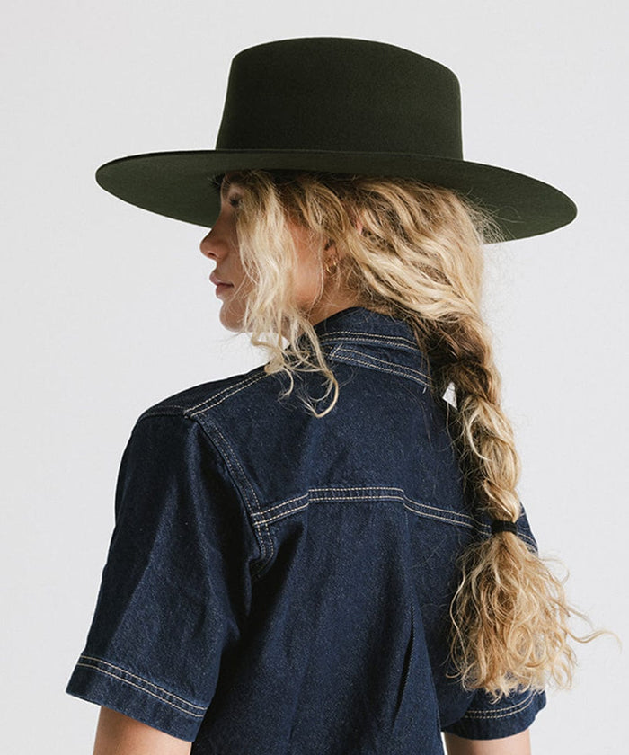 Woman wearing a dark green wide brim felt hat with a triangle crown and a denim jacket, facing sideways against a plain background #color_dark green