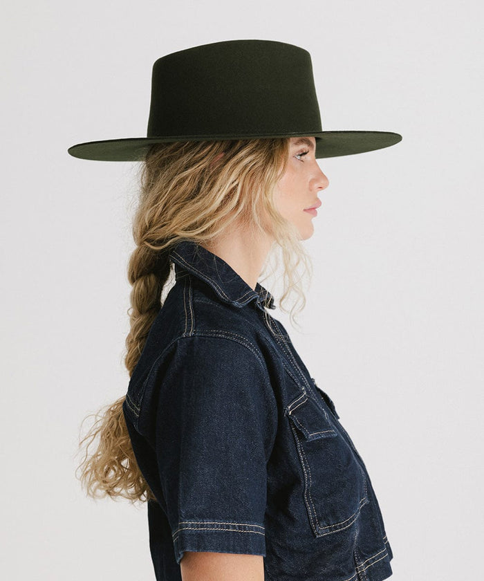 Woman wearing a dark green wide brim felt hat with a triangle crown and a denim jacket, facing sideways against a plain background #color_dark green