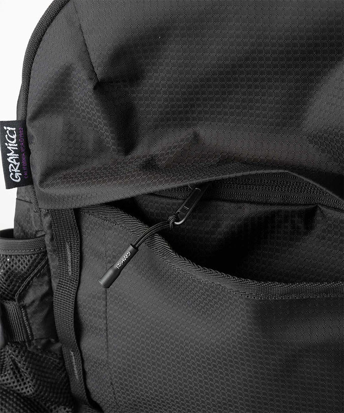 Close-up of Gramicci Day Pack 25L backpack in the color black against a light-tone background.