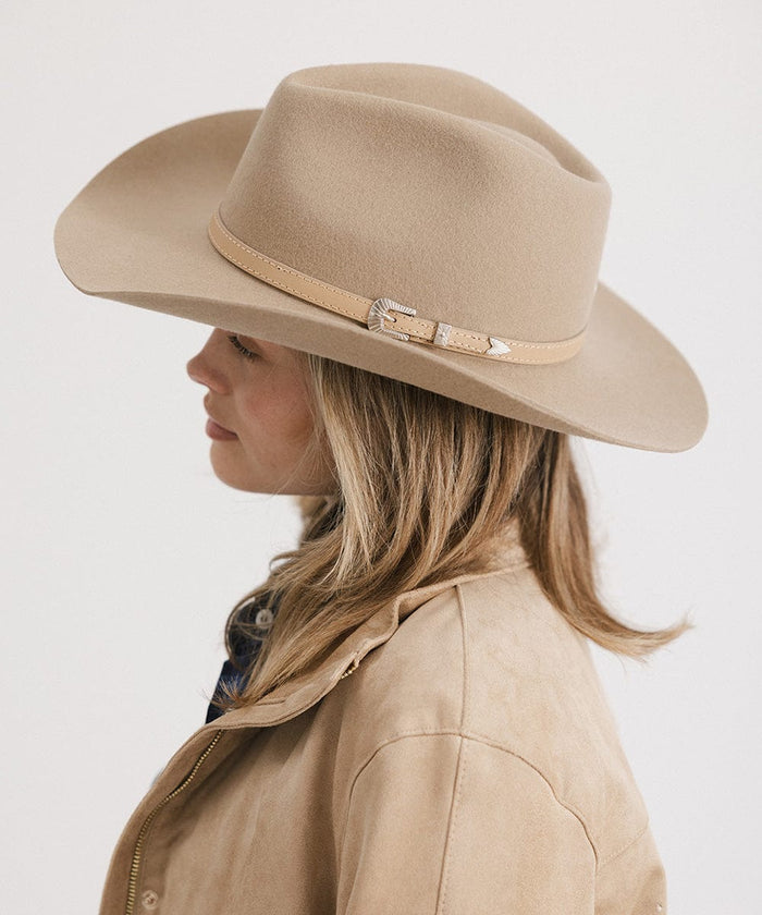 Woman wearing a tan cowboy hat with a hat band and a beige jacket, facing sideways against a plain background #color_tan