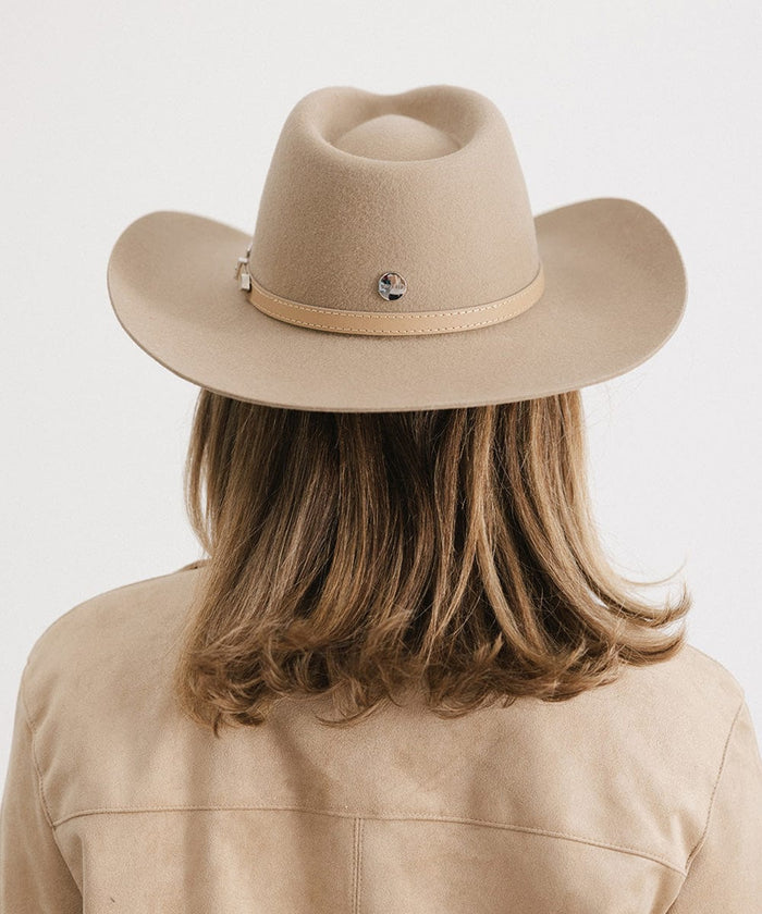 Woman wearing a tan cowboy hat with a hat band and a beige jacket, facing behind against a plain background #color_tan