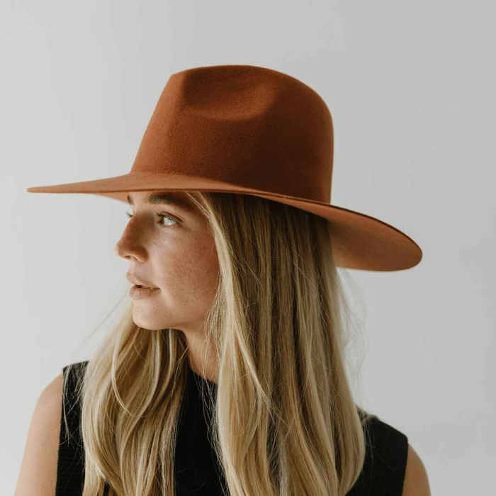 Woman wearing a terracotta colored wide brim hat against a plain background #color_terracotta