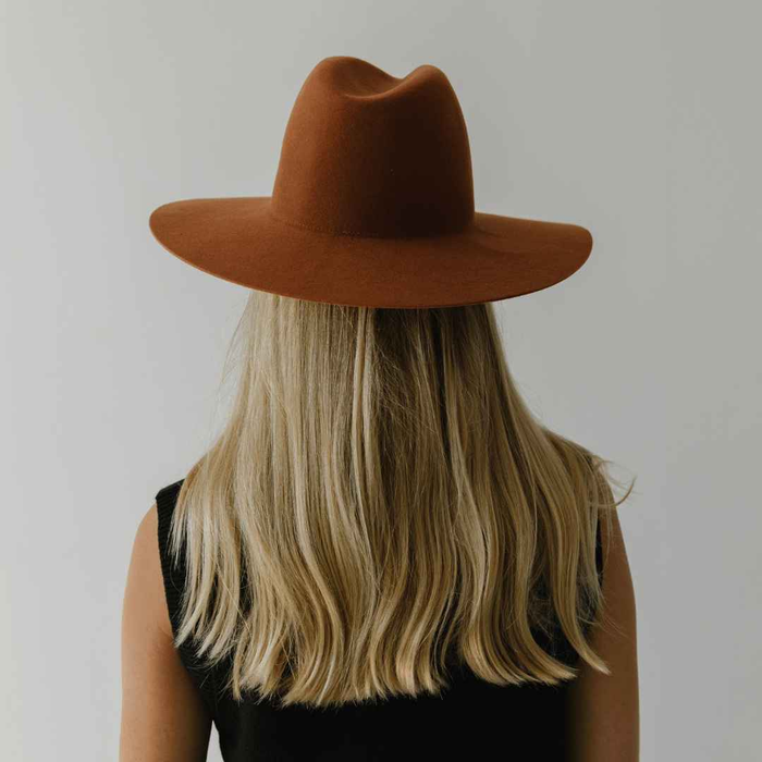 Person with long blonde hair wearing a terracotta colored wide brim hat against a plain background #color_terracotta