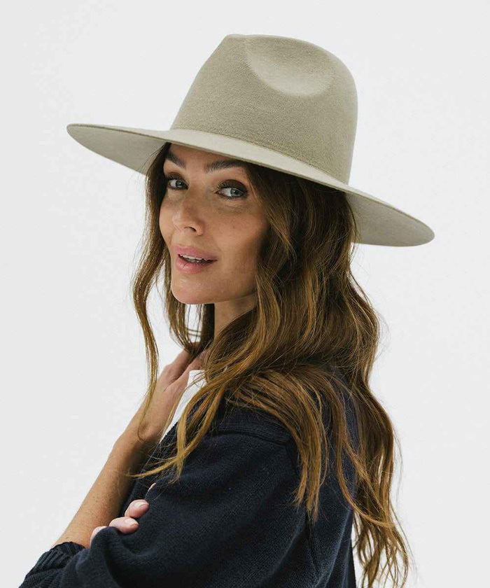 Woman wearing a sage colored wide brim fedora hat and a blue sweater, posing against a plain background #color_sage