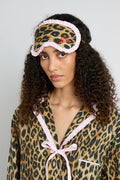 Woman wearing leopard print pajamas with a leopard print eye mask on her forehead