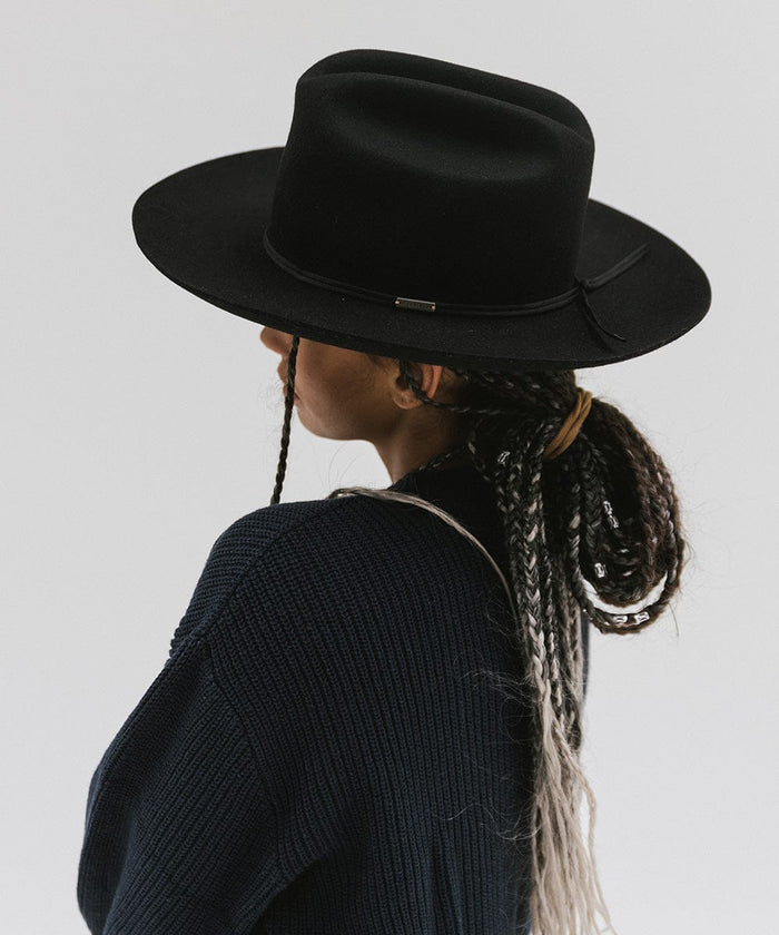 Person wearing a black Western hat with a classic cattleman crown and a black hat band, and a dark blue sweatshirt, facing sideways against a plain background  #color_black