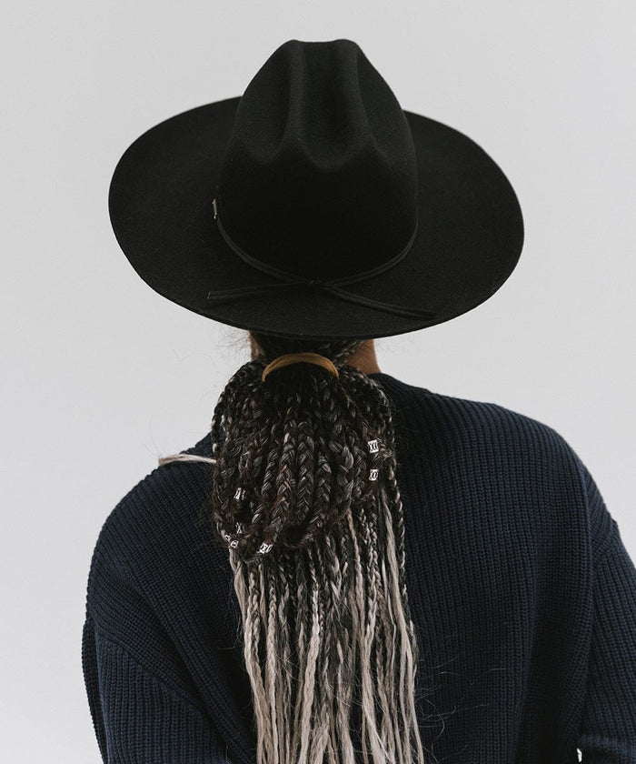 Person wearing a black Western hat with a classic cattleman crown and a black hat band, and a dark blue sweatshirt, facing behind against a plain background  #color_black
