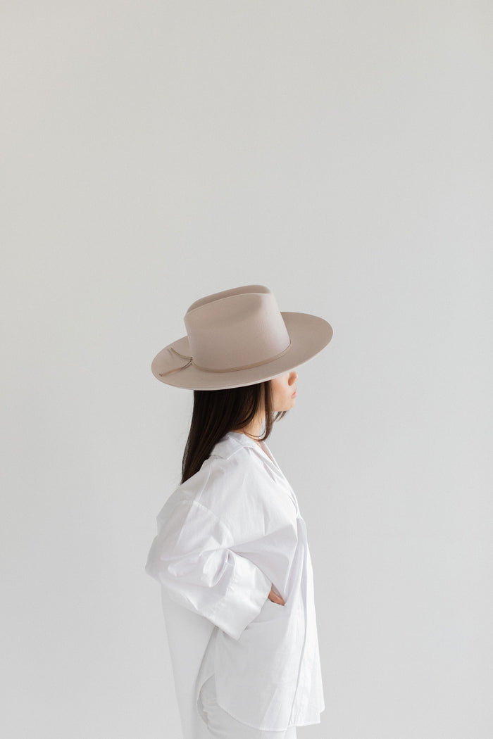 Woman wearing a ivory colored cowboy hat with a hat band and a white shirt, facing sideways against a plain background #color_ivory