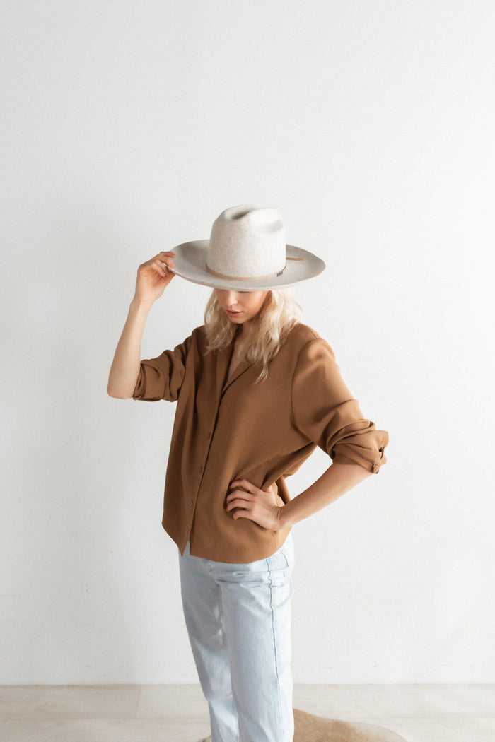 Woman wearing a mix grey colored wide brim felt hat with a hat band, a brown shirt and light blue jeans, posing against a plain background #color_mix grey