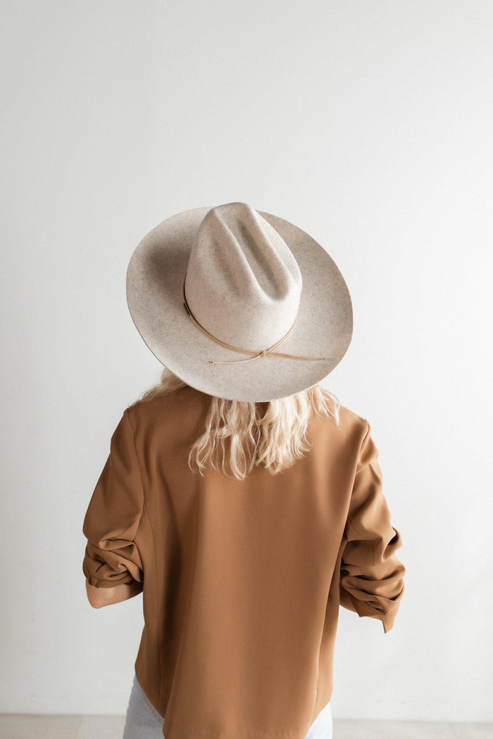 Woman wearing a mix grey colored wide brim felt hat with a hat band and a brown shirt, facing behind against a plain background #color_mix grey