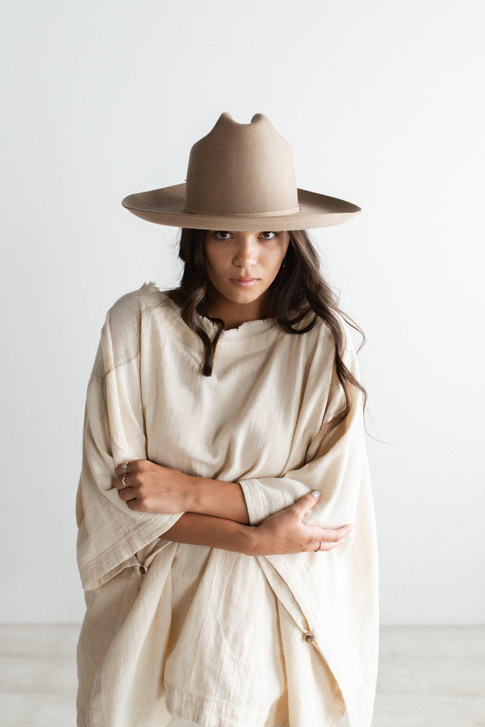 Woman wearing a tan cowboy hat with a hat band and a white dress against a plain background #color_tan