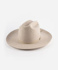 An ivory colored Western hat with a classic cattleman crown and an upturned brim. It features a tall crown and a stiff brim with a tonal grosgrain band and a brass Gigi Pip pin. #color_ivory