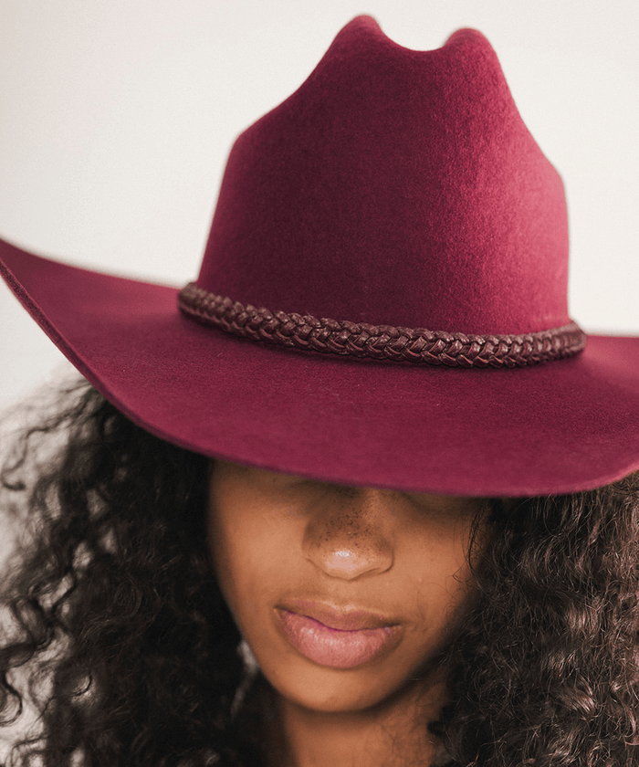 Woman wearing a maroon cowboy hat with a beige blazer against a white background #color_merlot