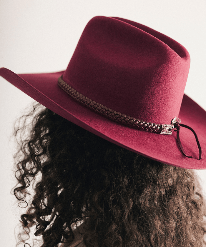 Woman wearing a maroon cowboy hat with a decorative band against a white background #color_merlot