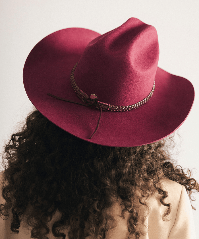 Woman wearing a maroon cowboy hat with a decorative band and a beige blazer against a white background #color_merlot