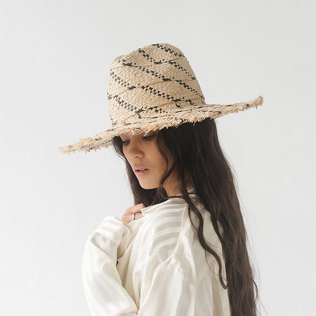 Woman wearing a natural colored straw hat with black patterns and a white shirt, posing sideways against a plain background #color_natural/black