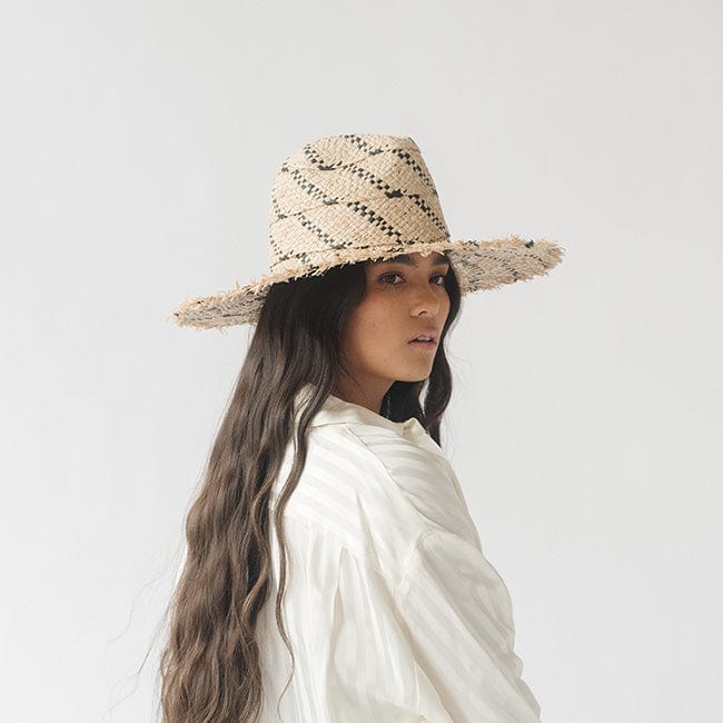 Woman with long hair wearing a natural colored straw hat with black patterns and a white shirt against a plain background #color_natural/black