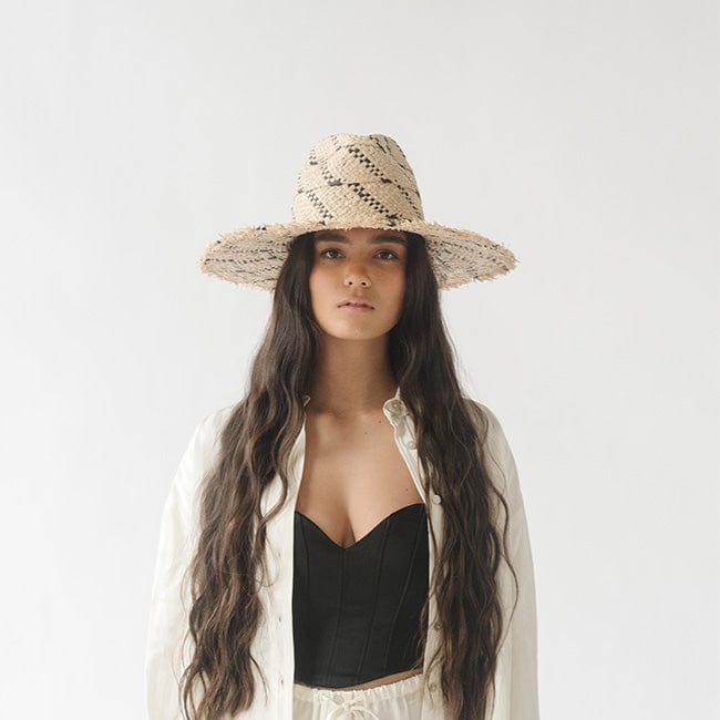 Woman wearing a natural colored straw hat with black patterns and a black top with a white shirt against a plain background #color_natural/black