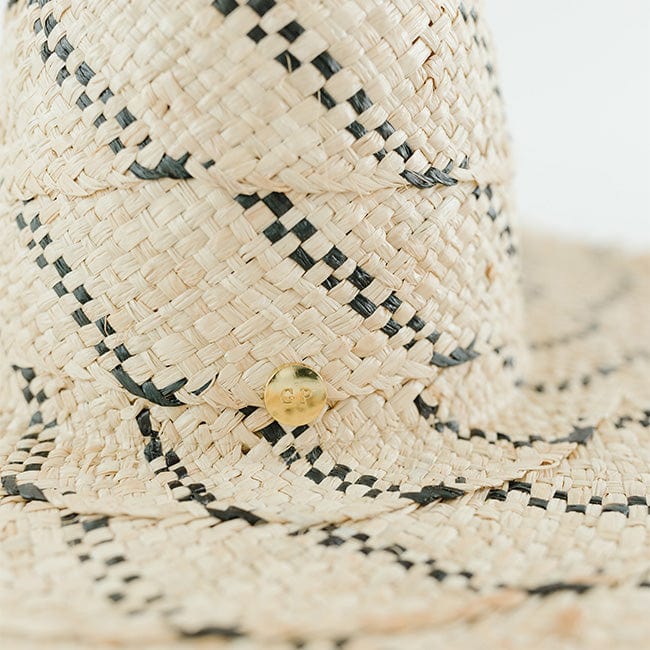 Close up image of a natural colored straw hat with black patterns against a plain background #color_natural/black