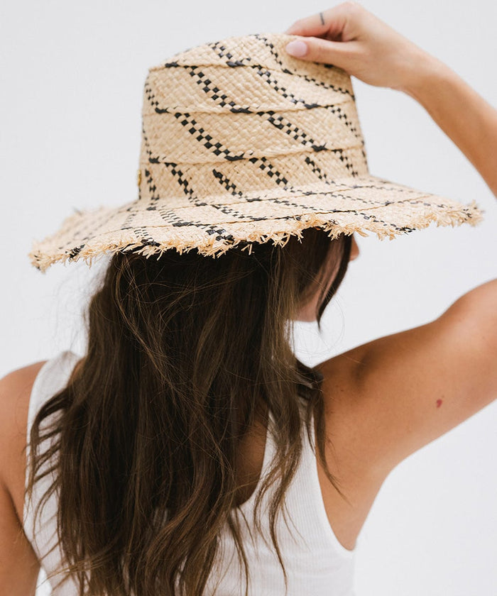 Woman wearing a natural colored straw hat with black patterns and a white top, facing behind against a plain background  #color_natural - black