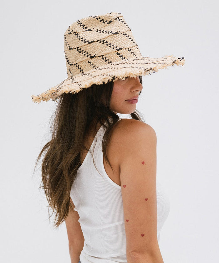 Woman wearing a natural colored straw hat with black patterns and a white top, posing sideways against a plain background  #color_natural - black