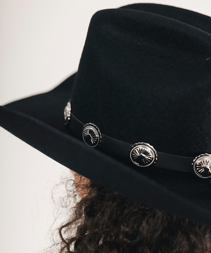 Black cowboy hat with decorative band and conchos on a plain background #color_black