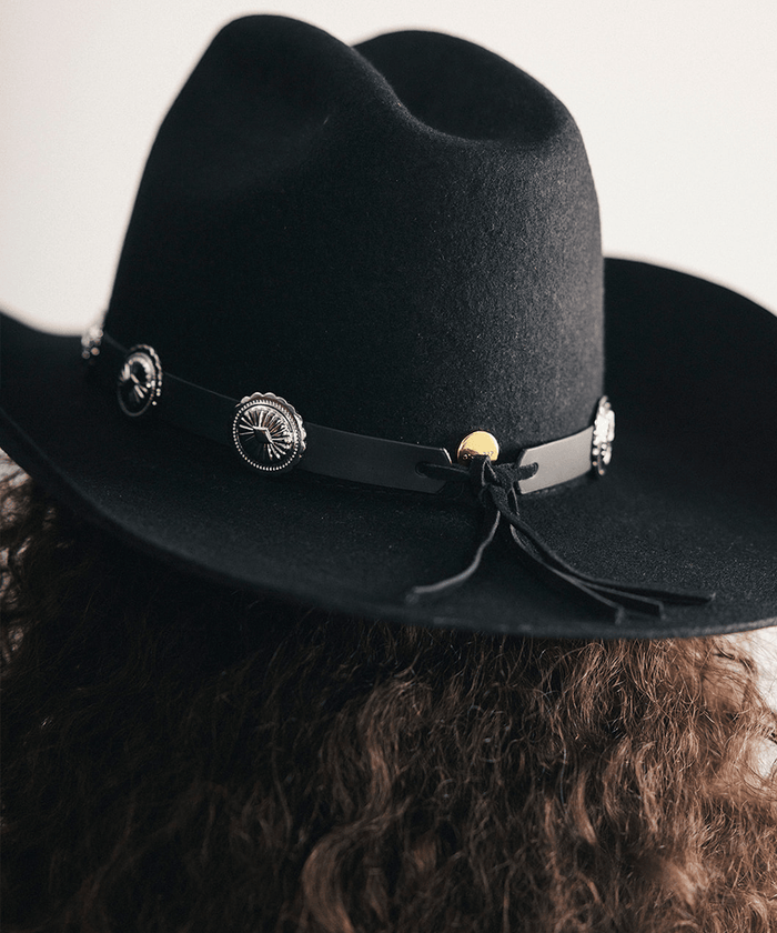 Black cowboy hat with decorative band and conchos on a plain background #color_black