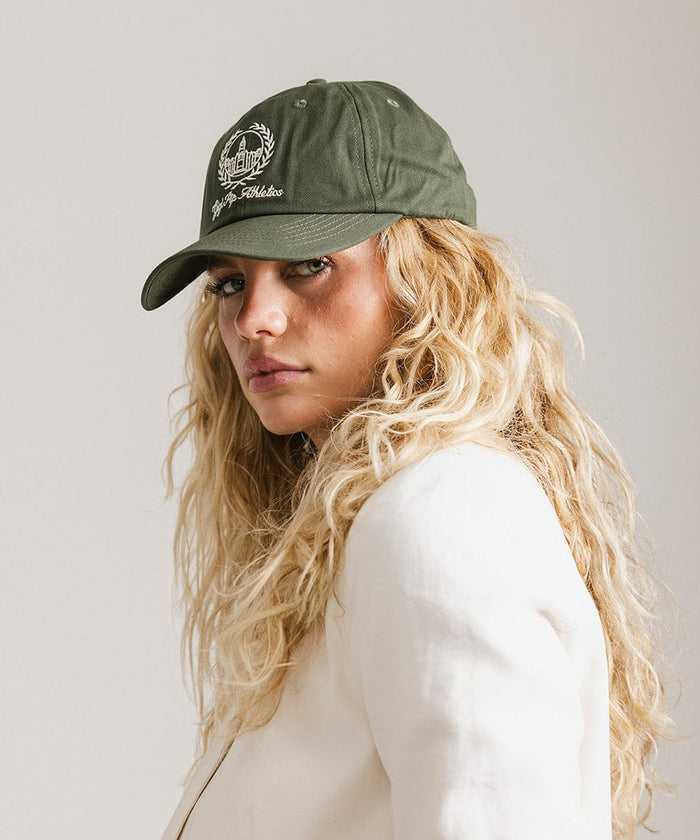 Woman wearing a dark green ball cap with a white logo and text and a white blazer, posing against a plain background  #color_dark green
