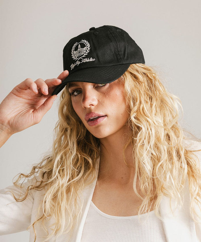 Woman wearing a black ball cap with a white logo and text and a white blazer, posing against a plain background  #color_black