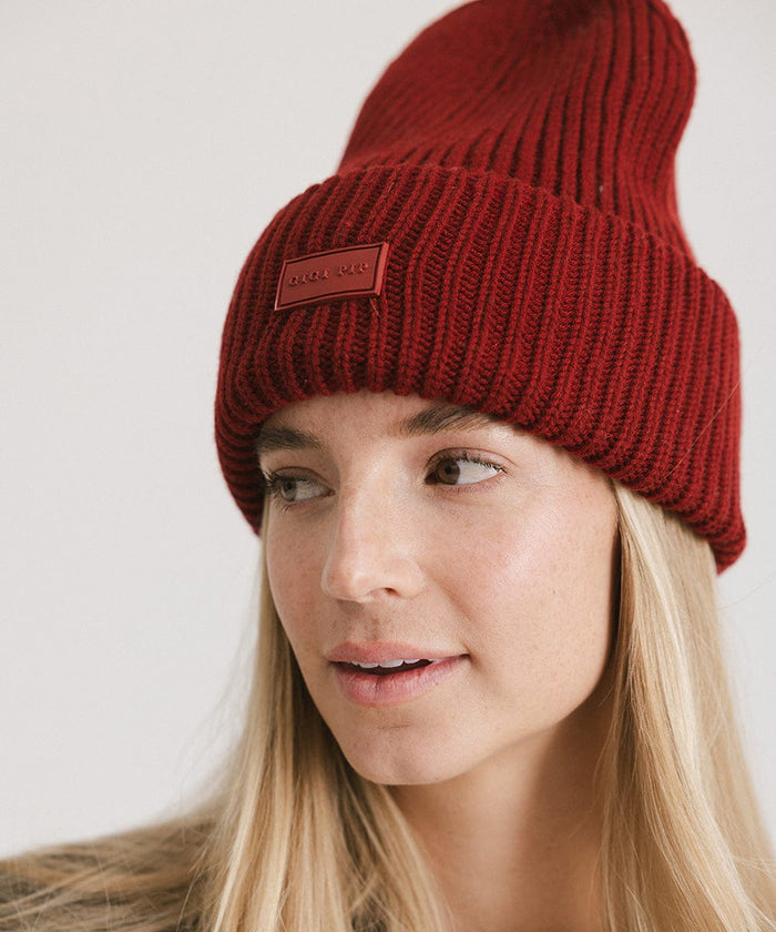 A woman wearing a burgundy chunky ribbed beanie, looking sideways against a plain background #color_burgundy