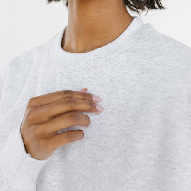 Person wearing an ash colored sweatshirt with the text 'GIGI PIP' in white against a plain background #color_ash-white