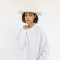 Woman wearing a white hat and an ash colored sweatshirt with the text 'GIGI PIP' in white against a plain background #color_ash-white
