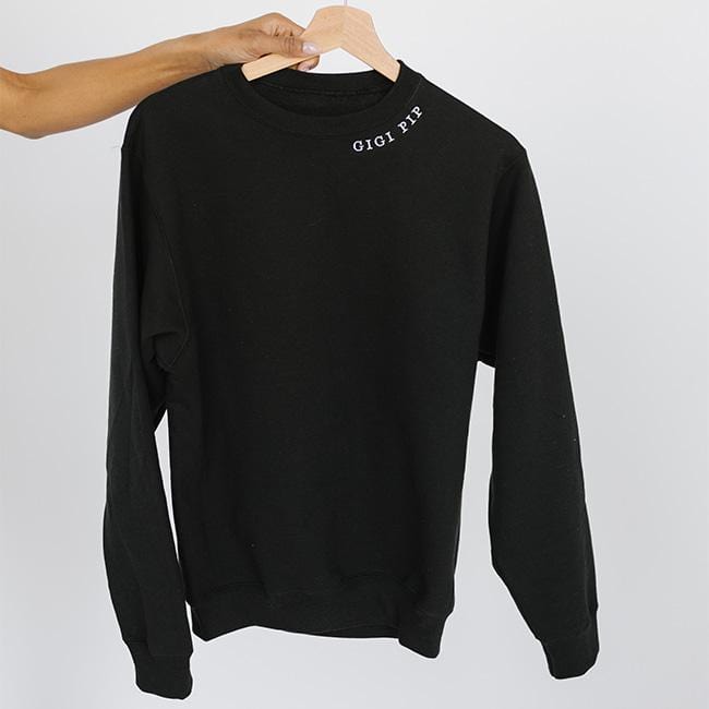 Person carrying a black sweatshirt with the text 'GIGI PIP' against a plain background #color_black
