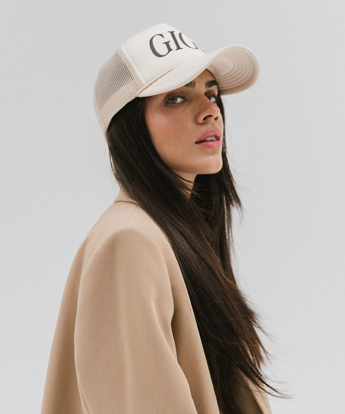 Woman wearing a cream cap with 'GIGI' text and a beige coat, posing sideways against a plain background  #color_cream
