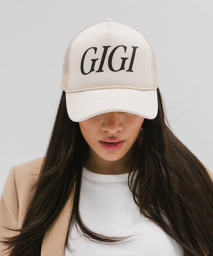 Woman wearing a cream cap with 'GIGI' text and a white top against a plain background  #color_cream