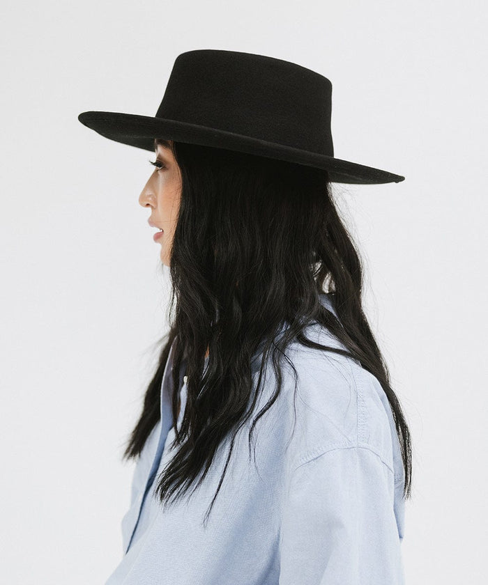 Woman wearing a black gambler hat and a blue shirt, facing sideways  against a plain background #color_black