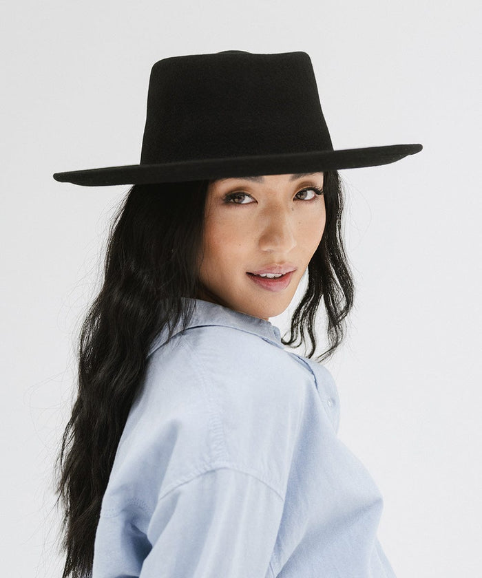 Woman wearing a black gambler hat and a blue shirt against a plain background #color_black