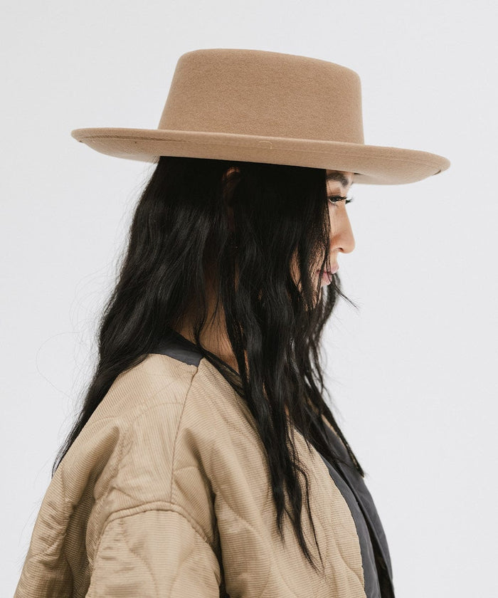 Woman wearing a brown gambler hat and a black top with a brown jacket, looking sideways against a plain background #color_brown