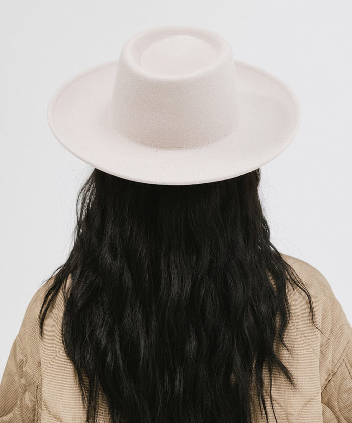 Woman wearing an ivory colored gambler hat and a brown jacket, facing behind against a plain background  #color_ivory