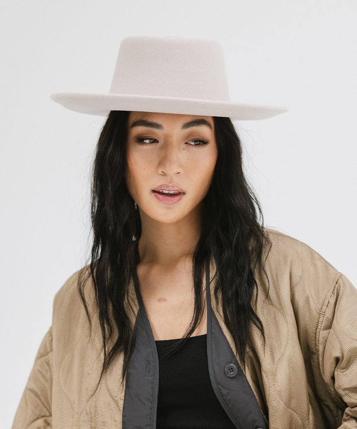 Woman wearing an ivory colored gambler hat and a brown jacket against a plain background  #color_ivory