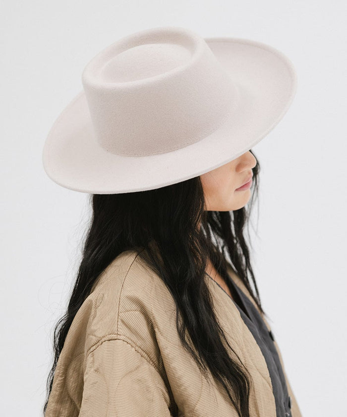 Woman wearing an ivory colored gambler hat and a brown jacket, facing sideways against a plain background  #color_ivory