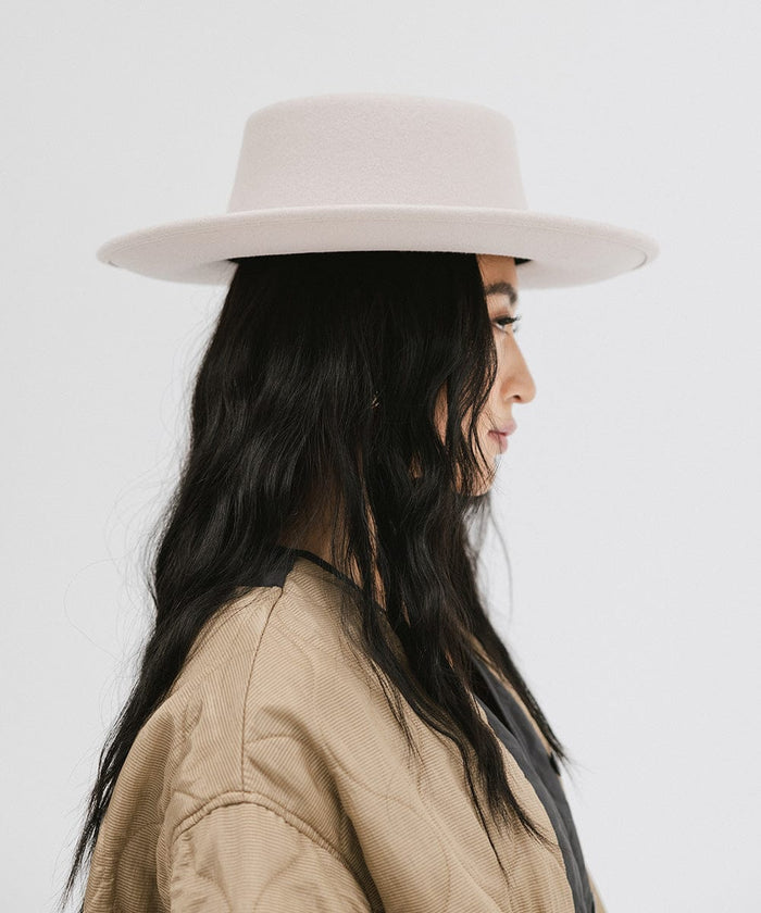 Woman wearing an ivory colored gambler hat and a brown jacket, facing sideways against a plain background  #color_ivory