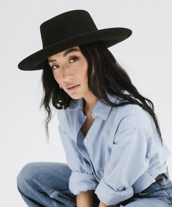 Woman wearing a black gambler hat, a blue shirt and jeans against a plain background #color_black