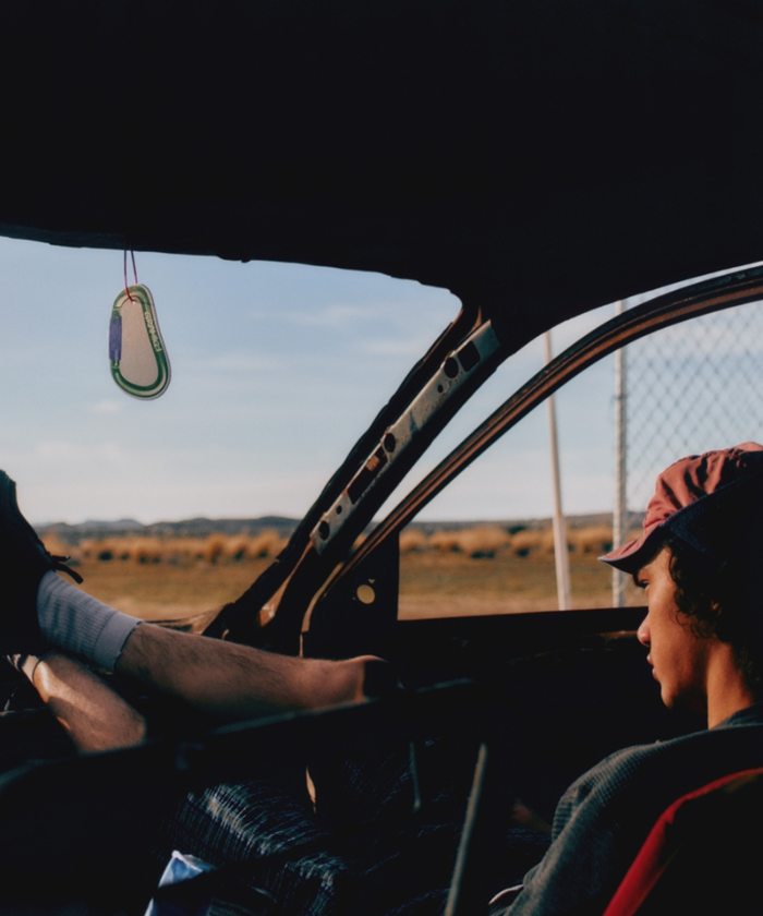 Photo of a model sitting in a car with an Olive Gramicci & retaW Carabiner Car Tag air freshener hanging from the rears-view mirror.