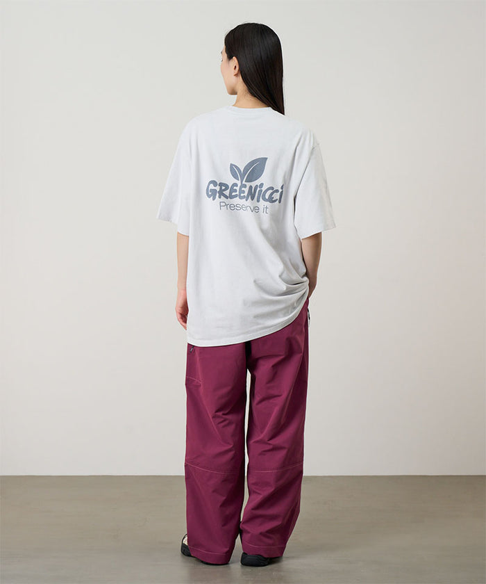 Back 
view of a model wearing a smoke colored Gramicci Greenicci Tee with a graphic and purple pants on a light tone background.