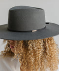 Woman wearing a grey hat with a black grosgrain hat band facing sideways against a plain background #color_black