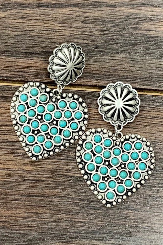 Antique silver heart-shaped drop earrings featuring turquoise-look stone accents and western concho details. Statement cowgirl earrings perfect for rodeos, country concerts, western outfits, and everyday boutique styling.