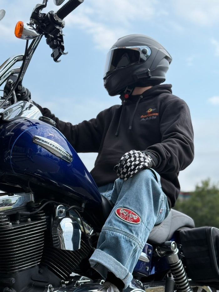 Person sitting on a motorcycle wearing a helmet and checkered gloves with a clear sky background