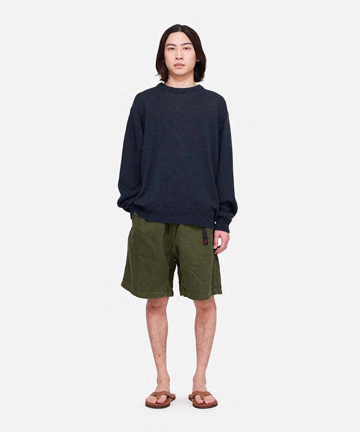 Model wearing hemp olive colored Gramicci Hemp G-Shorts and a black sweater on a light-tone background.